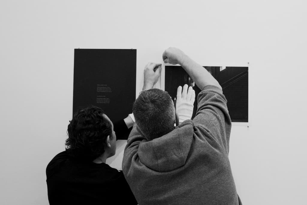 Two collaborators installing Lenâpa works on a gallery wall.