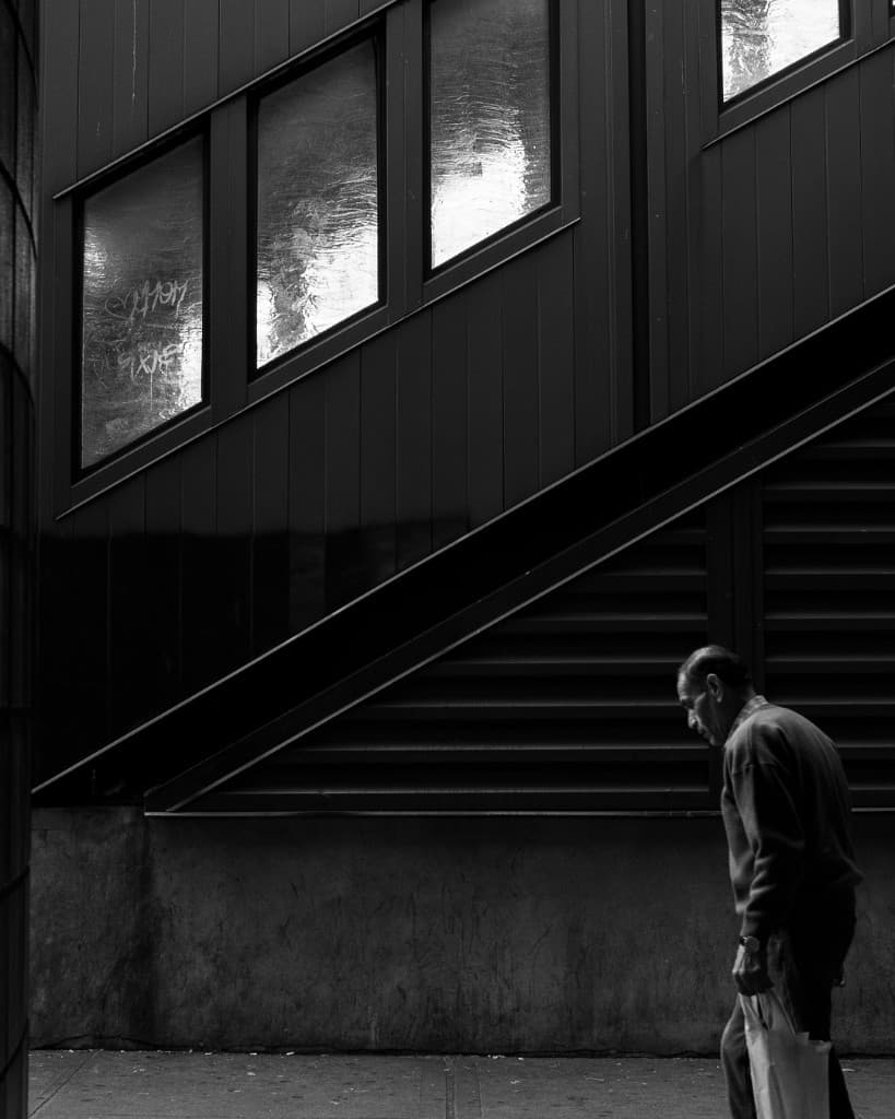 Figura junto a una escalera diagonal en entorno urbano oscuro.