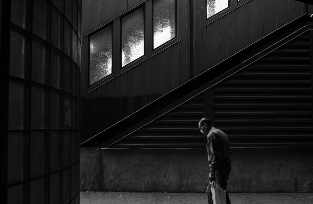 Figura caminando junto a una escalera urbana en sombra.