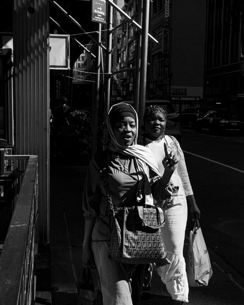 Dos figuras avanzan por una calle en sombra junto a Herald Square.